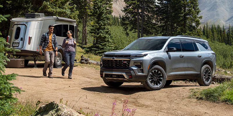 Chevrolet SUV parked near a campsite with a trailer and outdoor adventure scenery.