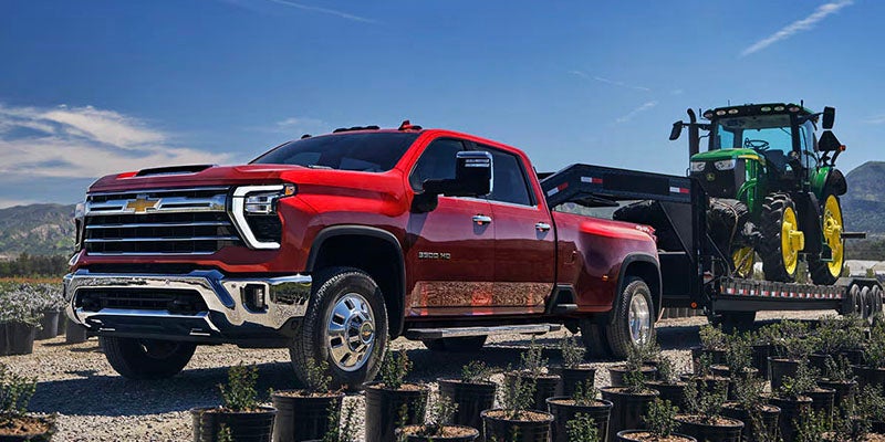 Chevrolet Silverado HD truck towing a trailer with agricultural equipment outdoors.