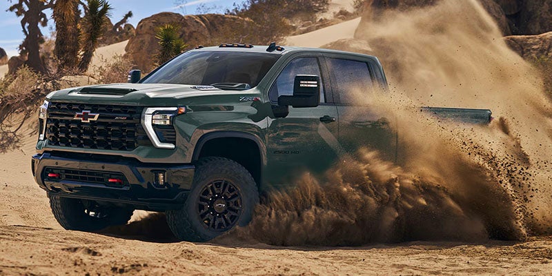 Chevrolet Silverado HD truck driving through desert terrain with dust trail.